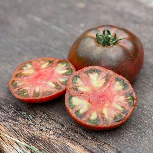 Dark purple heirloom tomato with sliced view showing green and pink interior, on wooden surface